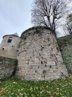 Old round stone tower and fortress wall with bare trees and grass under a grey sky