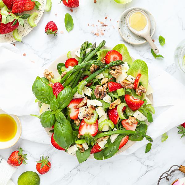 Colorful salad with strawberries, asparagus, cheese cubes, walnuts, and fresh basil on a white plate
