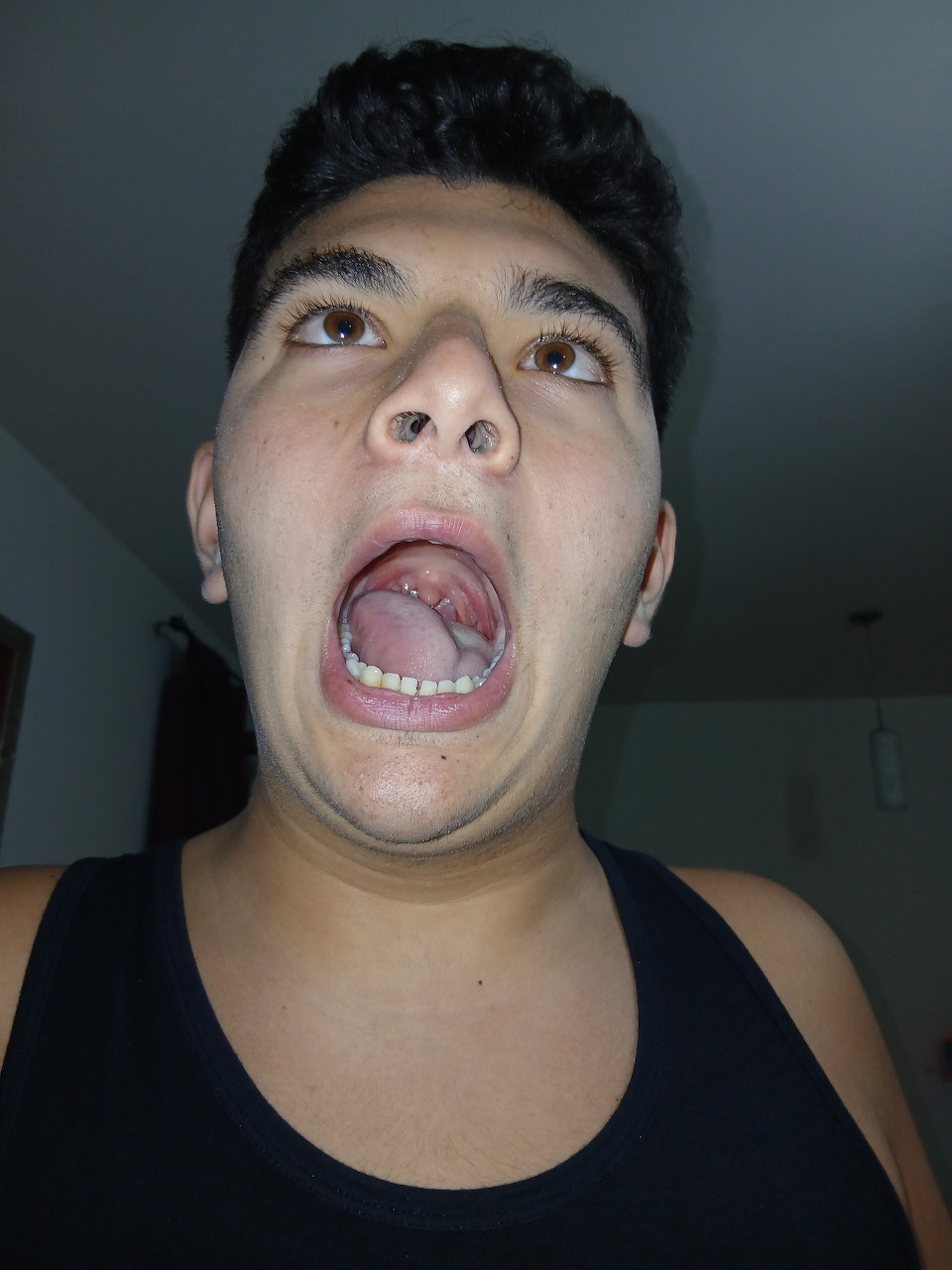 Young man looking up with mouth wide open, wearing a black tank top indoors
