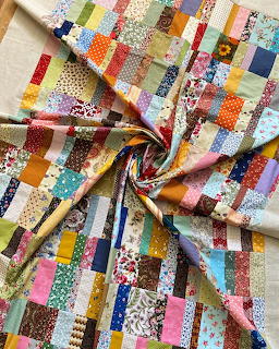 Colorful patchwork quilt with small fabric squares in various patterns, gathered in center