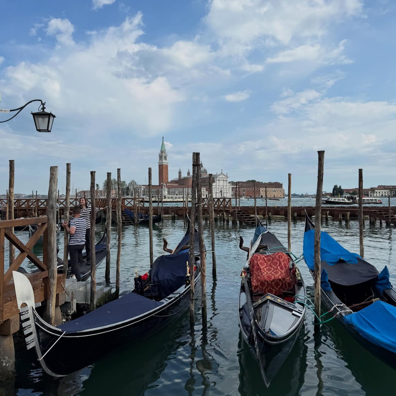 Gondolas moored at wooden posts in Venice with basilica across water and blue sky