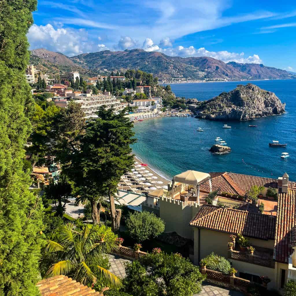 Coastal view of Taormina, Sicily with rooftops, bay, boats, rocky shore, and mountains