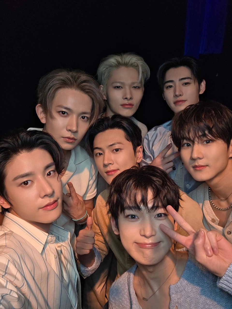 Seven members of K-pop group Enhypen posing together in a close group selfie with peace signs