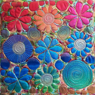 Colorful handmade textile art with embroidered flower shapes in various bright colors arranged in a folk art pattern