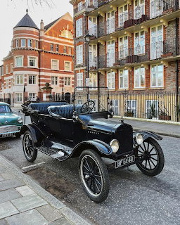 Black vintage open-top car parked on a London street with red brick buildings behind