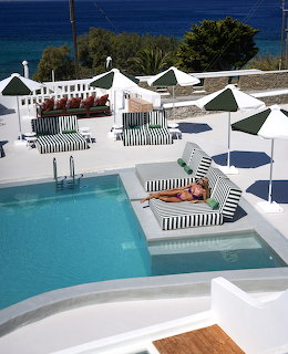 White resort terrace with turquoise pool, striped sun loungers, and ocean view
