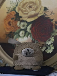 Handmade knitted hedgehog stuffed animal in front of a floral painting with roses