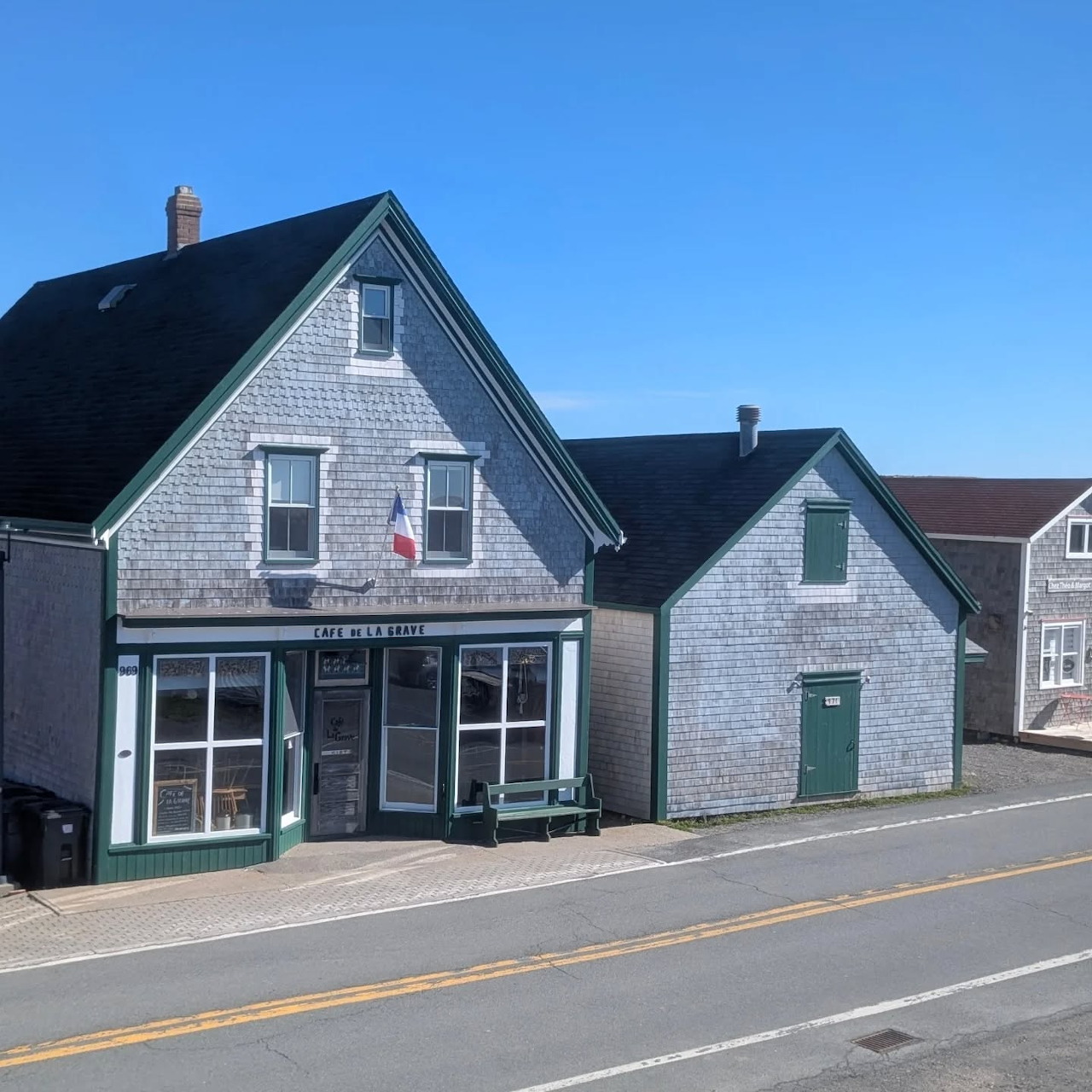Gray shingled boutique and small houses beside a quiet road under a blue sky