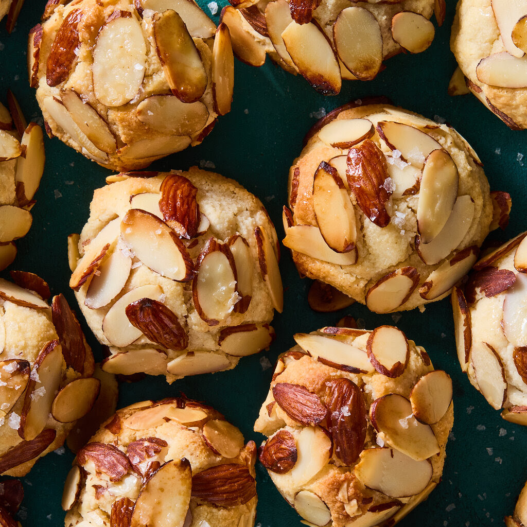 Golden cookies with sliced almonds on teal background