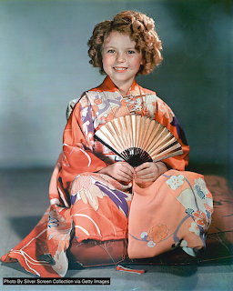 Young girl in orange kimono with curly hair holding decorative fan in vintage portrait photo