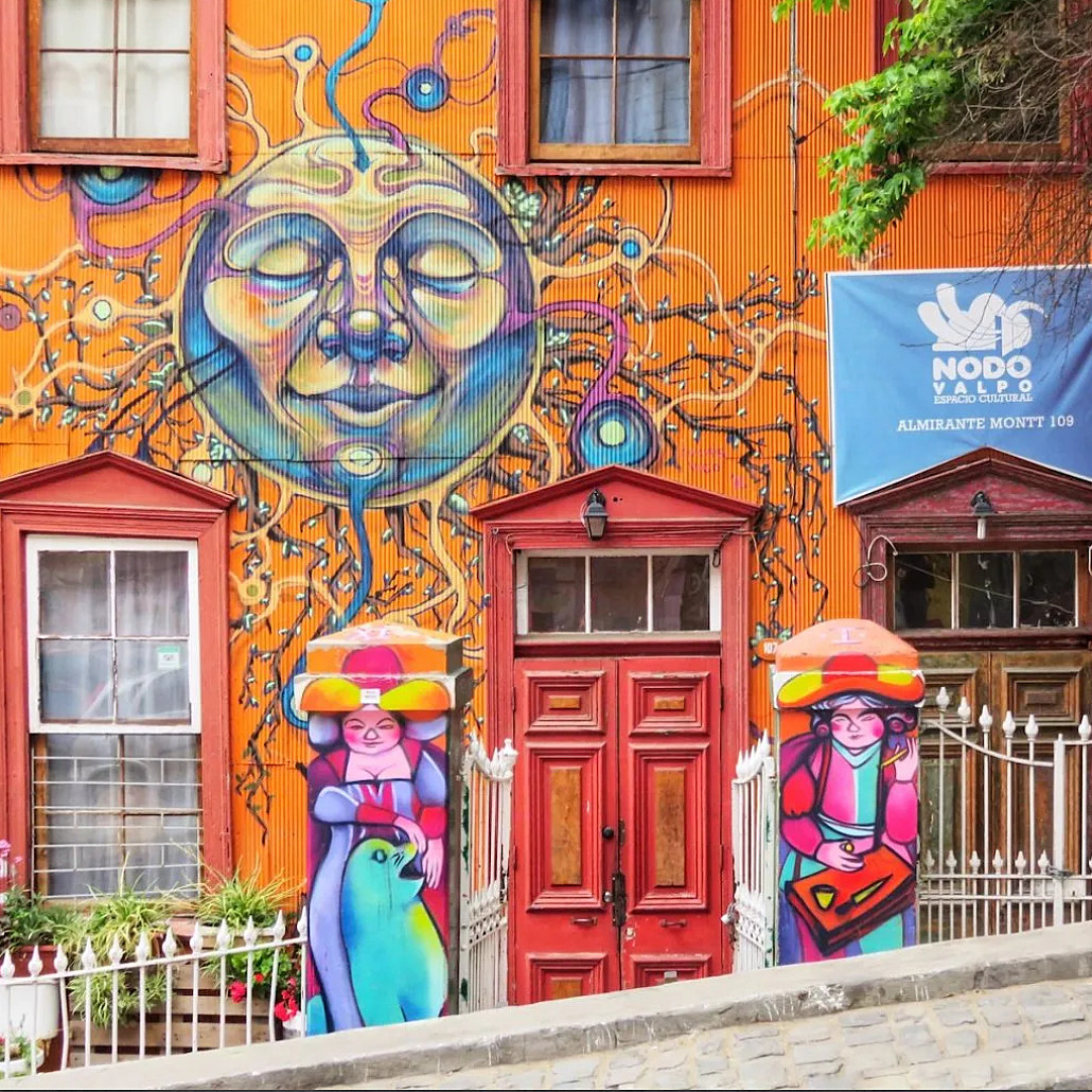 Orange house with large smiling sun mural and colorful painted figures on facade