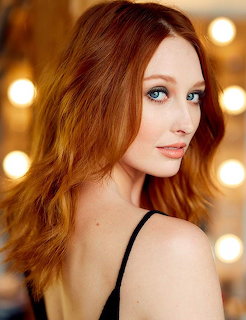 Portrait of woman with long red hair and blue eyes looking over shoulder against bokeh lights
