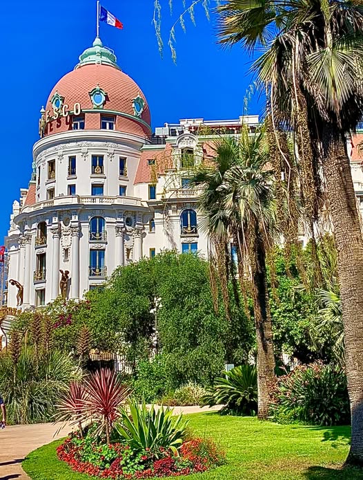 Pink-domed Hotel Negresco with palm trees and garden under blue sky