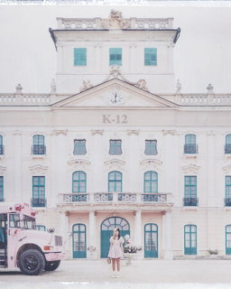 Girl and pink school bus in front of a large white K-12 building in pastel tones