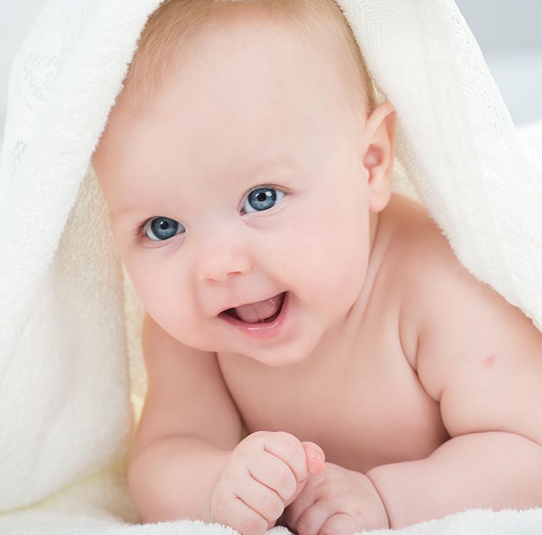 Smiling baby with blue eyes under a white blanket