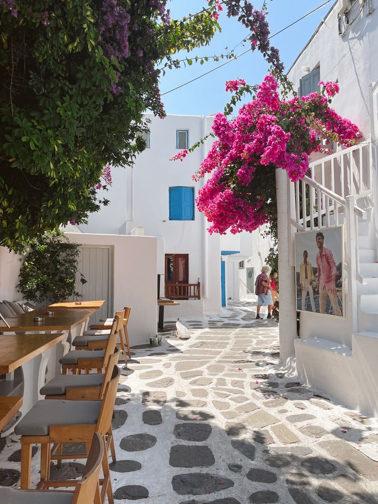 Whitewashed alley in Mykonos with pink bougainvillea, stone pavement, and outdoor cafe tables