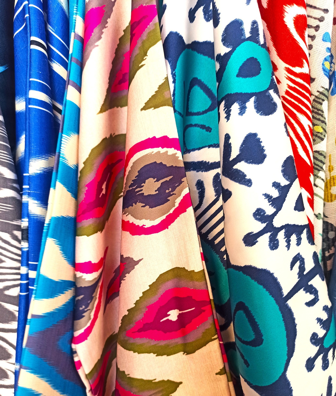 Hanging ethnic scarves with colorful geometric patterns and traditional designs in red, blue, and pink