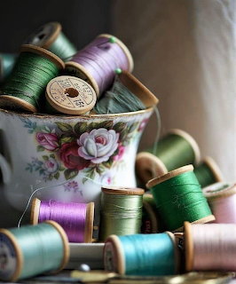 Vintage wooden thread spools in various colors arranged in an antique floral china bowl on a wooden table
