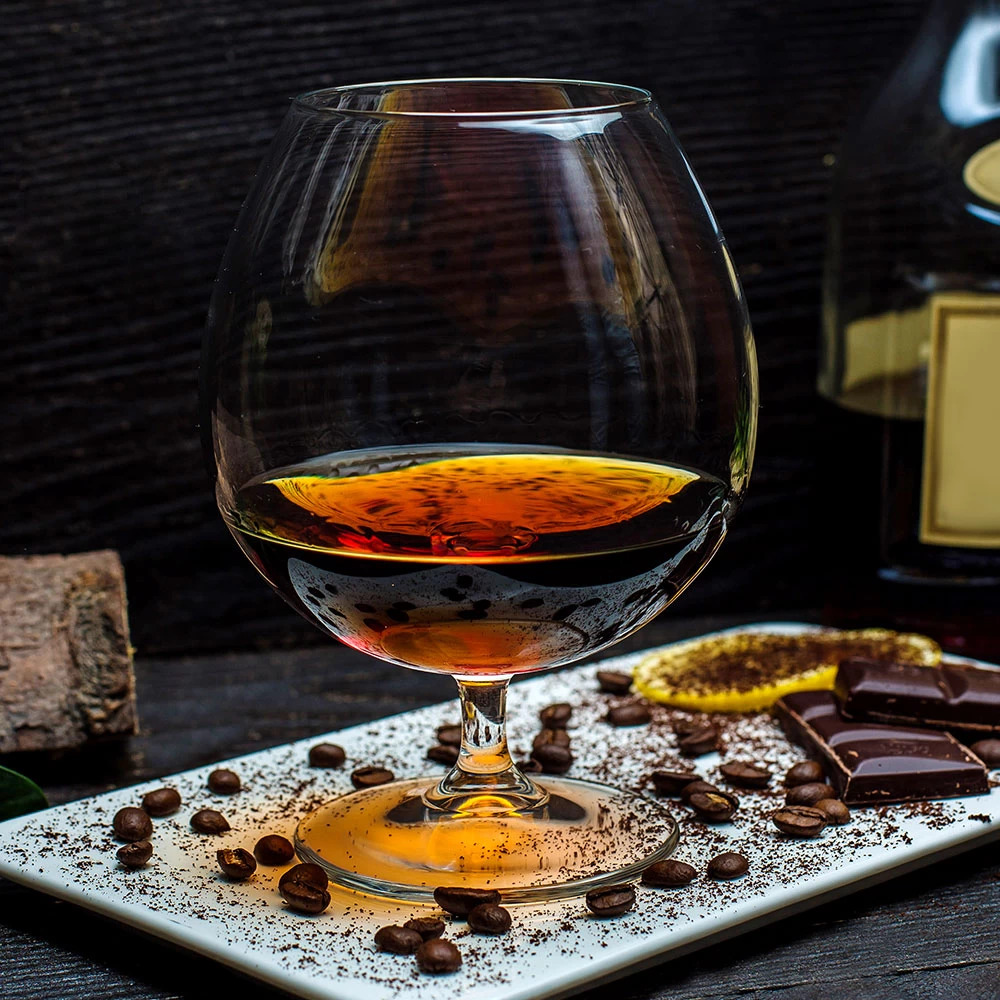 Brandy snifter with amber spirit on white plate decorated with chocolate and coffee beans