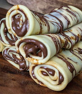 Stack of rolled crepes drizzled with chocolate sauce on wooden board