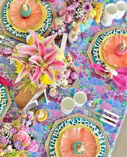 Overhead view of a colorful floral table with lilies, plates, cups, and small desserts