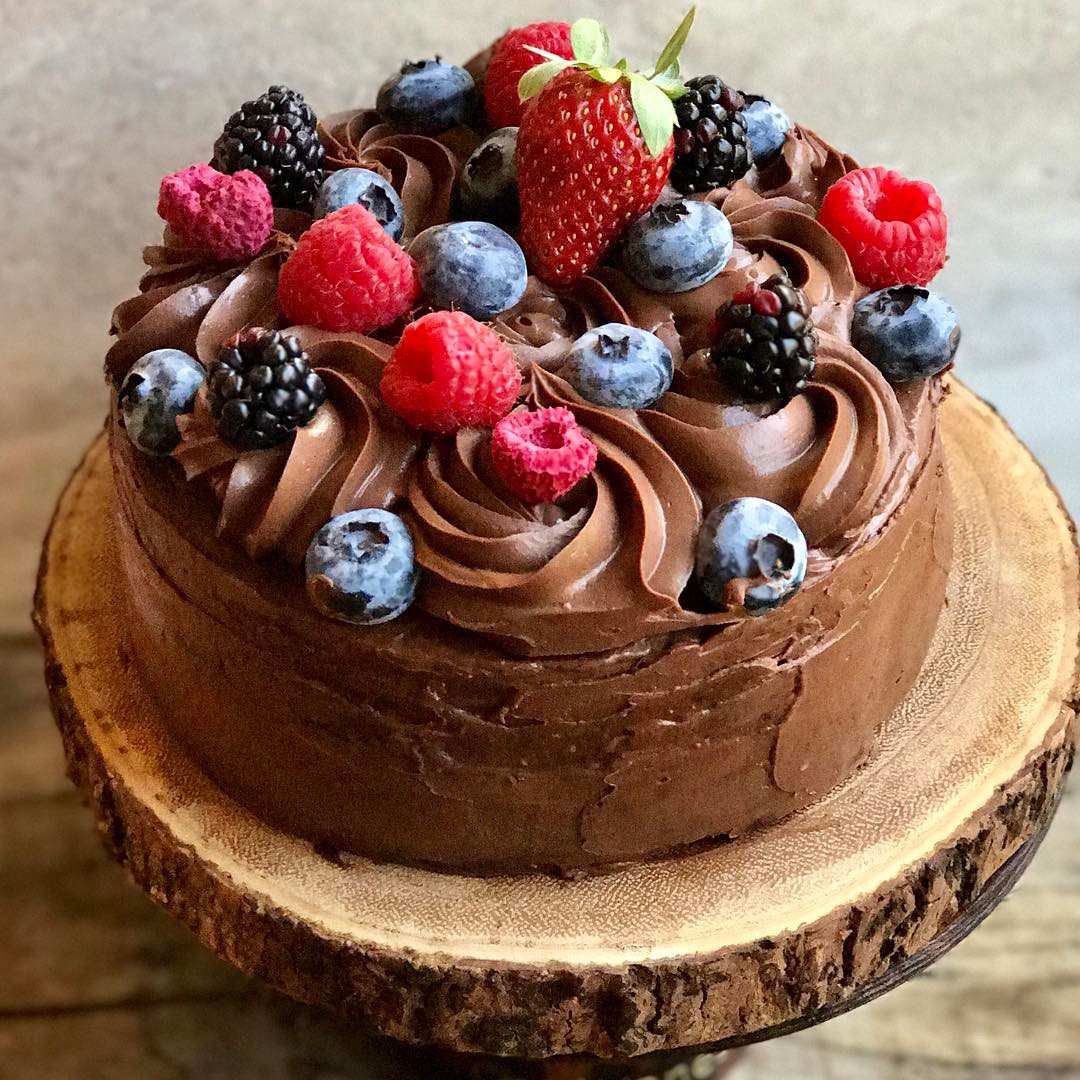 Chocolate cake with chocolate frosting swirls and mixed berries including strawberries, raspberries, blueberries, and blackberries