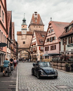 Medieval German town street with timber-framed buildings, tower gate, and vintage black car on cobblestones