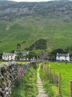 Path between stone walls and cottages with a green hillside behind