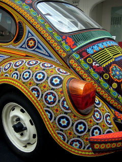 VW Beetle car decorated with colorful Huichol beadwork patterns featuring geometric circles and lines