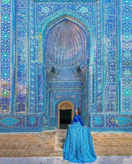 Woman in blue dress facing ornate blue tiled mosque entrance with Islamic arch