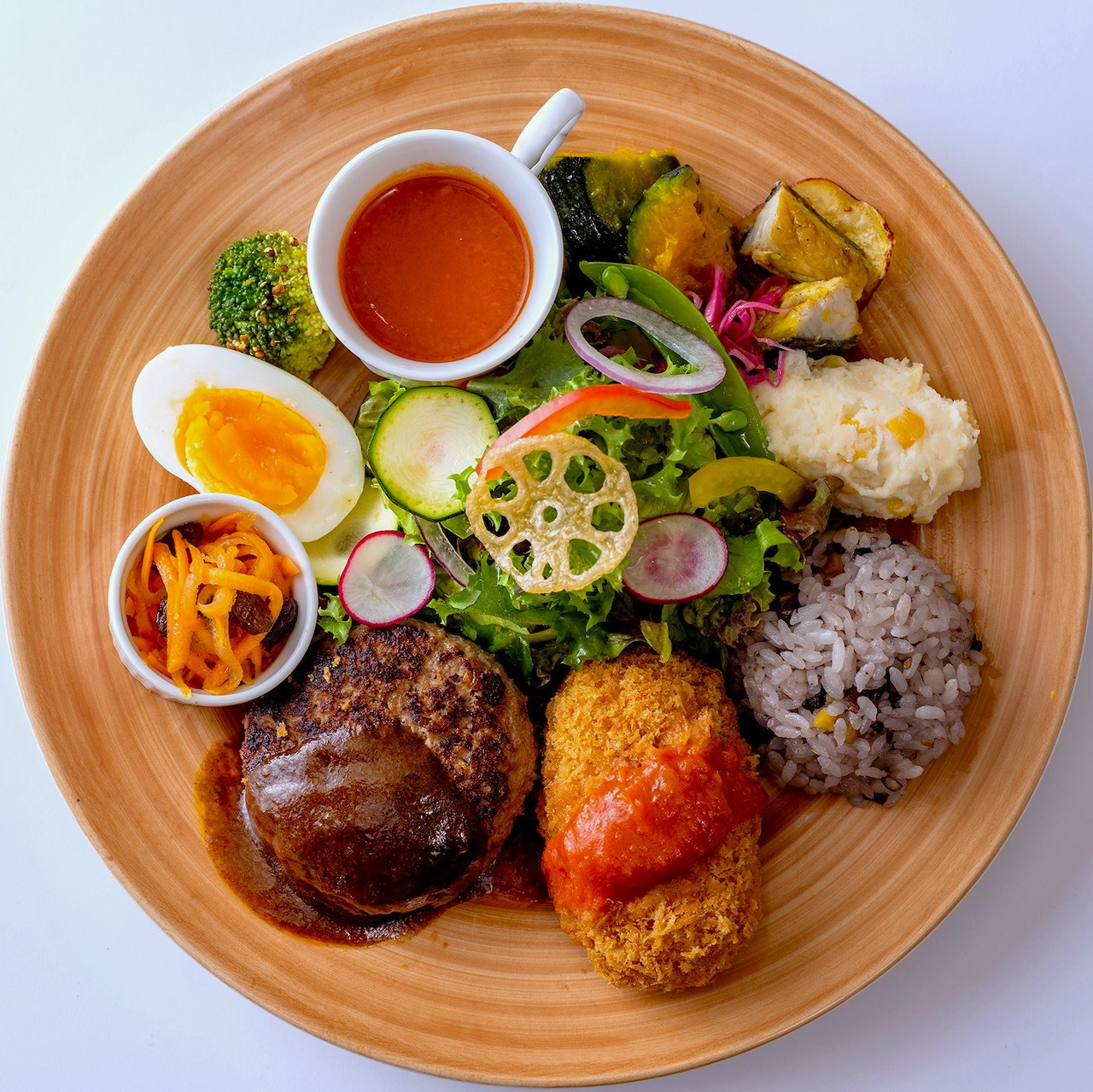 Overhead view of colorful Japanese lunch plate with hamburg steak, croquette, vegetables, egg, and rice on wooden dish