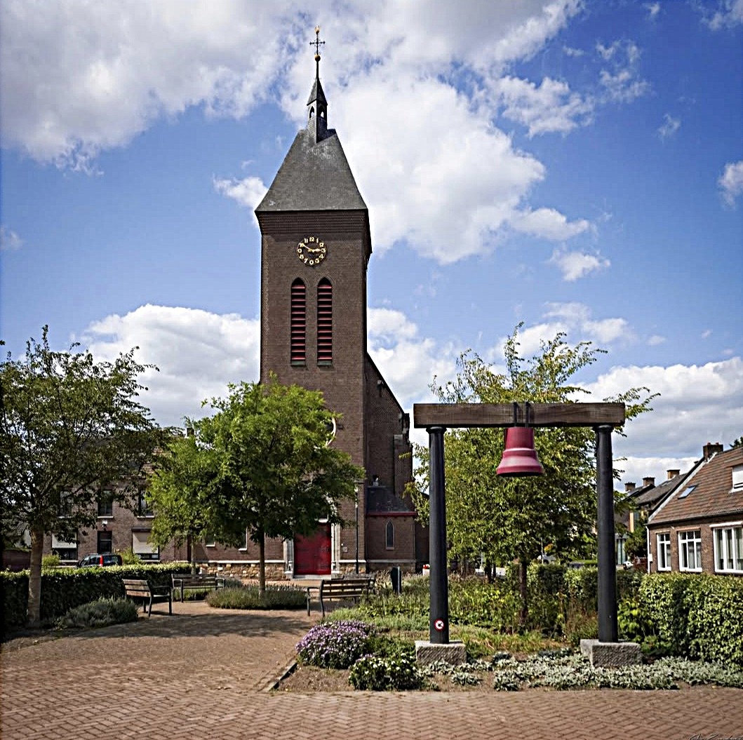 Stone church tower with steeple in village square with flowering garden and traditional houses