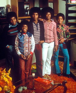 Five young men in colorful 1970s clothing posing together in a retro interior