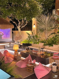 Outdoor terrace with pink cushions around fire pit, palm plants, and evening lighting