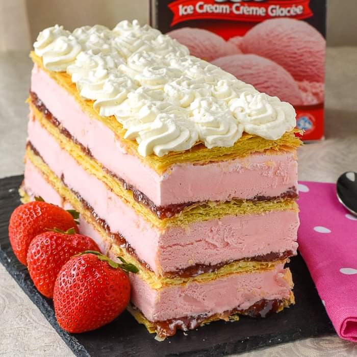 Thick slice of pink strawberry ice cream cake with white whipped cream and fresh strawberries