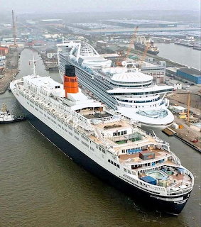 Aerial view of two large cruise ships docked at a port with industrial surroundings
