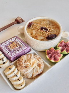 Korean food spread with soup bowl, rice cakes, sweet potato, and figs on white table