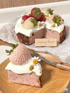 Slice of pink strawberry cake with cream, berries, and daisy flowers on wood
