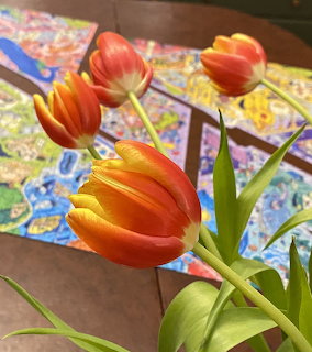 Orange and red tulips on a wooden table with a colorful puzzle behind them