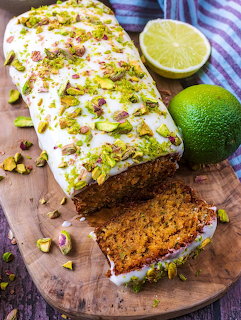 Glazed loaf cake with pistachios on a wooden board beside a halved lime and a whole lime