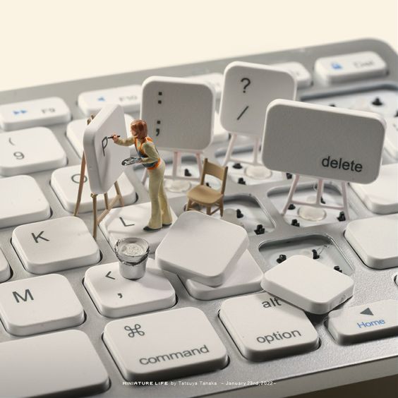 Miniature wooden figure standing on a white keyboard with loose keycaps scattered around