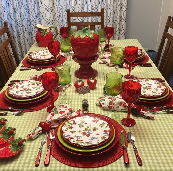 Festive dining table with floral plates, red and green glasses, and a fruit bowl centerpiece