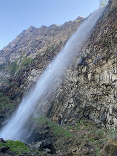 Tall waterfall streaming down a dark layered rock cliff face with green vegetation