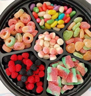Black compartment tray with assorted colorful candies including jelly beans, gummy rings, and marshmallows