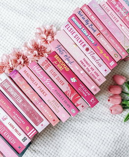 Stack of pink romance novels arranged diagonally with pink tulips and cherry blossoms on white background