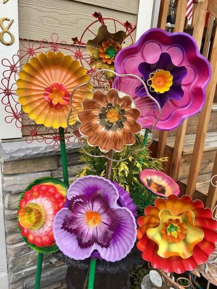 Vibrant metal flower art in purple, orange, and pink arranged with green stems against weathered wood wall