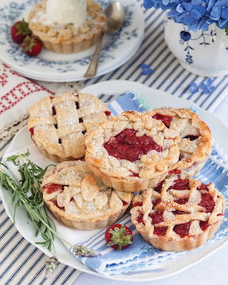 Three mini strawberry tarts with decorative lattice pastry crusts on white plates with blue striped napkin
