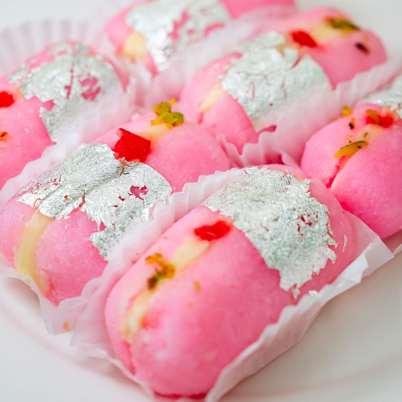 Close-up of pink cream-filled cakes with silver leaf topping on a white plate