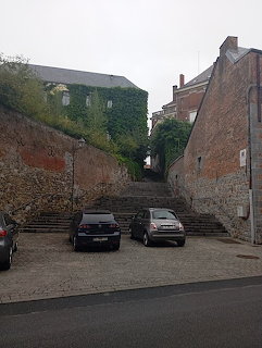 Narrow cobblestone alley with parked cars between tall brick walls and old buildings