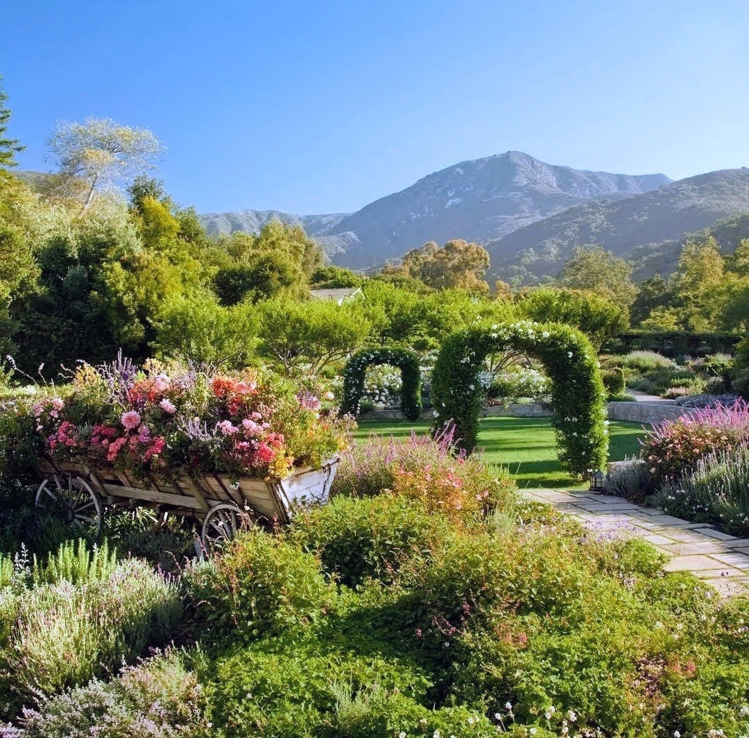 Scenic garden with vibrant flowers, green hedges, stone path, and mountains in background